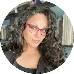 Woman with long, dark, curly hair and red glasses smiles, wearing a black top.