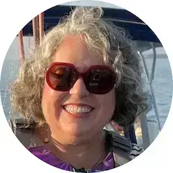 Smiling woman with grey curly hair and red sunglasses, wearing a life vest on a boat.
